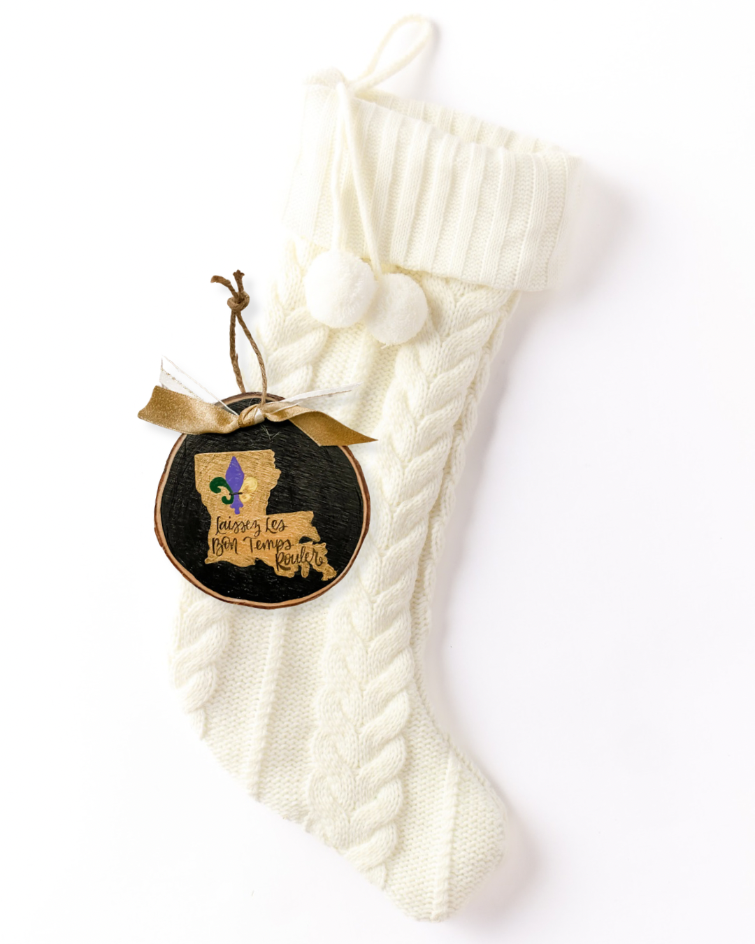 Hand-painted wood slice ornament with a gold Louisiana silhouette, a purple, green, and gold fleur de lis, hand-lettered "Laissez Les Bon Temps Rouler," and gold ribbon on a white knit stocking