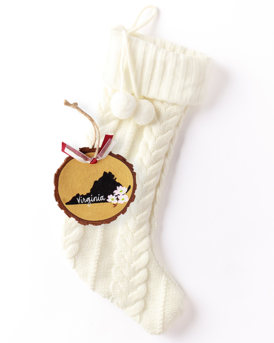 Hand-painted wood slice ornament with a black Virginia silhouette on gold, white dogwood blossoms, white hand-lettered "Virginia," and red and white ribbon on a white knit stocking