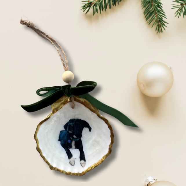 Personalized scallop shell ornament with a black puppy photo, gold edges, and green velvet bow on a cream holiday backdrop.