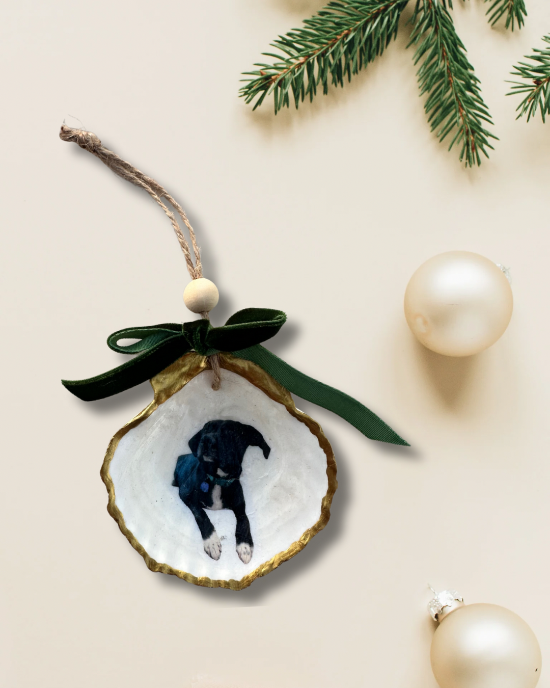 Personalized scallop shell ornament with a black puppy photo, gold edges, and green velvet bow on a cream holiday backdrop.
